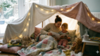 Child and parent sitting inside a cozy blanket fort reading a book during winter indoor play.