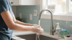 Parent washing hands at the kitchen sink to prevent norovirus spread.