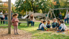 Shy child observing other children playing before joining a group activity at the playground.